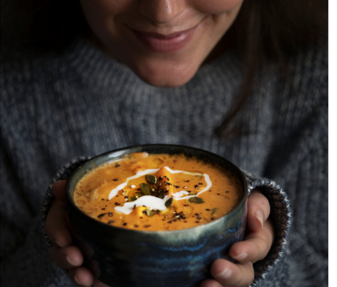 Woman gripping a mug of hearty soup